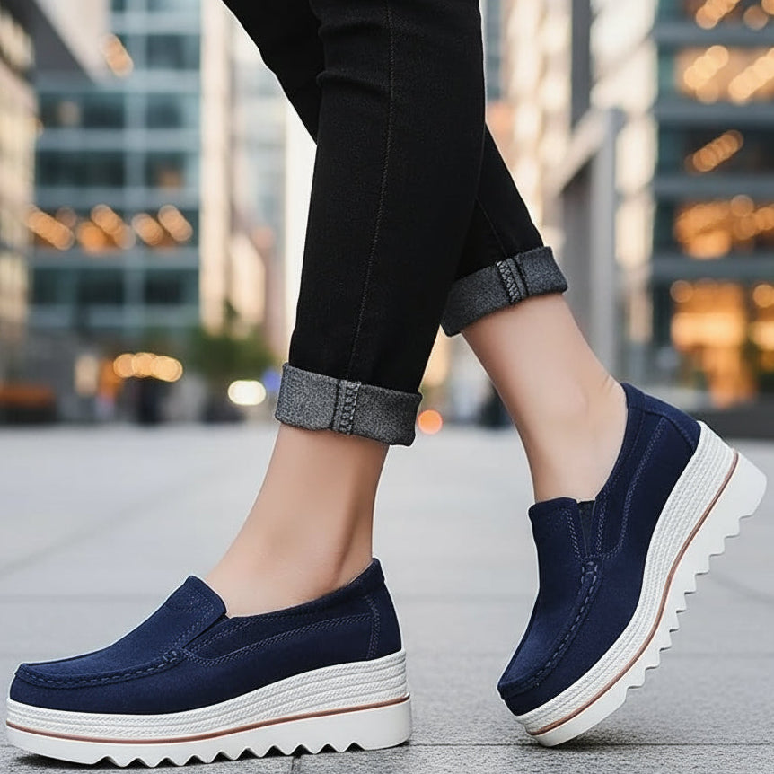 Navy blue loafers with white soles worn by a person on a wooden floor.
