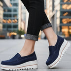 Navy blue loafers with white soles worn by a person on a wooden floor.