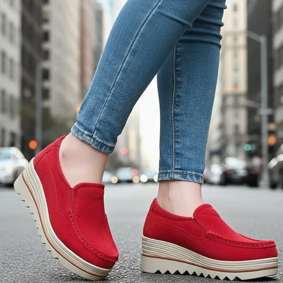 Red platform shoes worn with blue jeans on a light gray floor.
