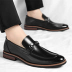 Black leather loafers worn with black pants on a light gray background